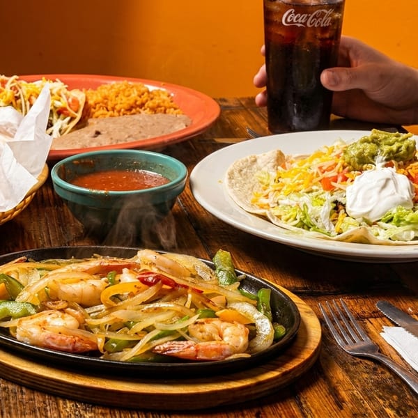 A table laden with Mexican dishes including shrimp fajitas, tacos, nachos, and a taco salad.